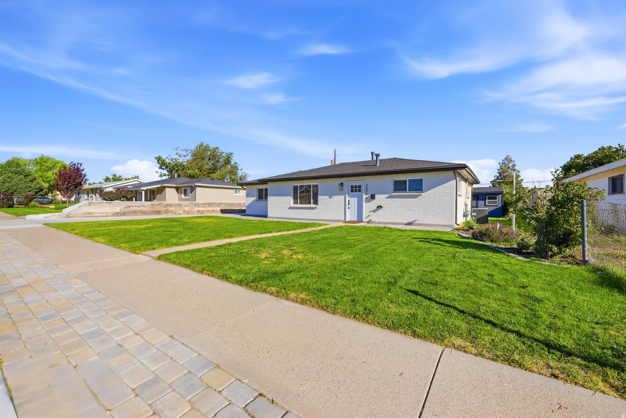 White brick exterior with a dark roofline, green lawn, concrete walkway, and paver stone hardscaping