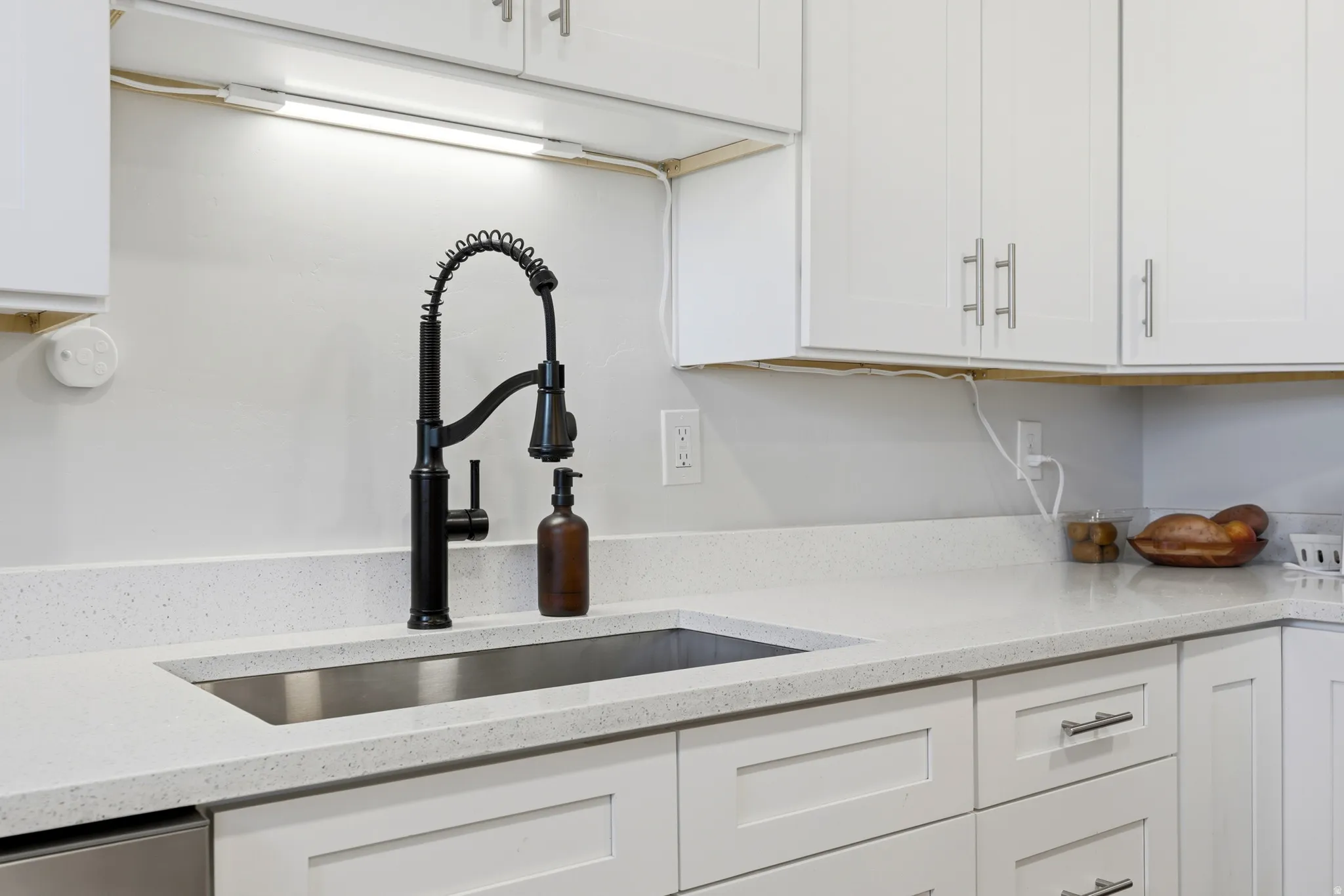 White shaker-style cabinetry with brushed nickel hardware, light-toned speckled countertops, undermount stainless steel sink, and a matte black pull-down faucet
