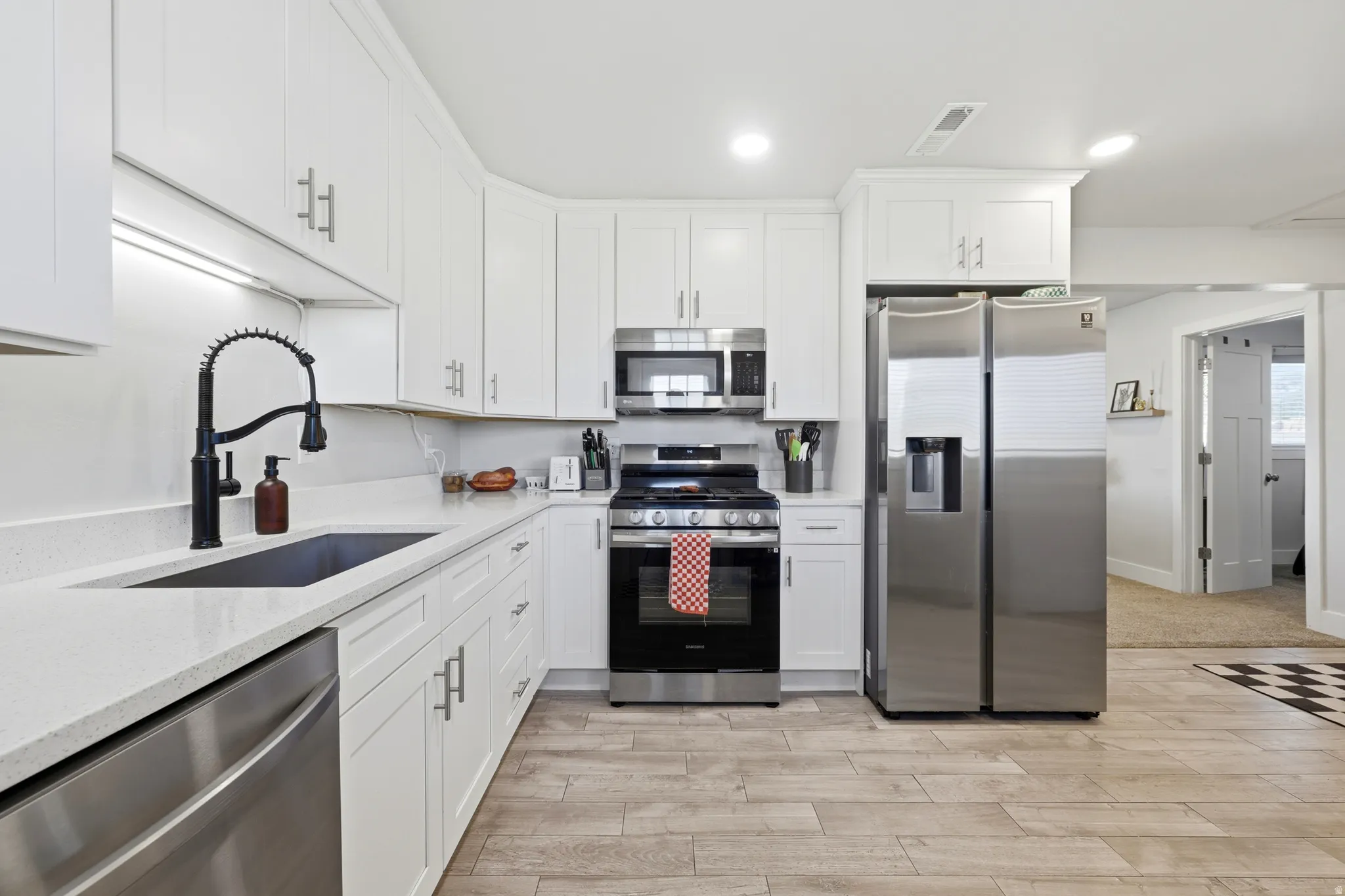 Modern kitchen featuring white cabinetry, light countertops, wood-finish flooring, a stainless steel refrigerator, and a matte black faucet