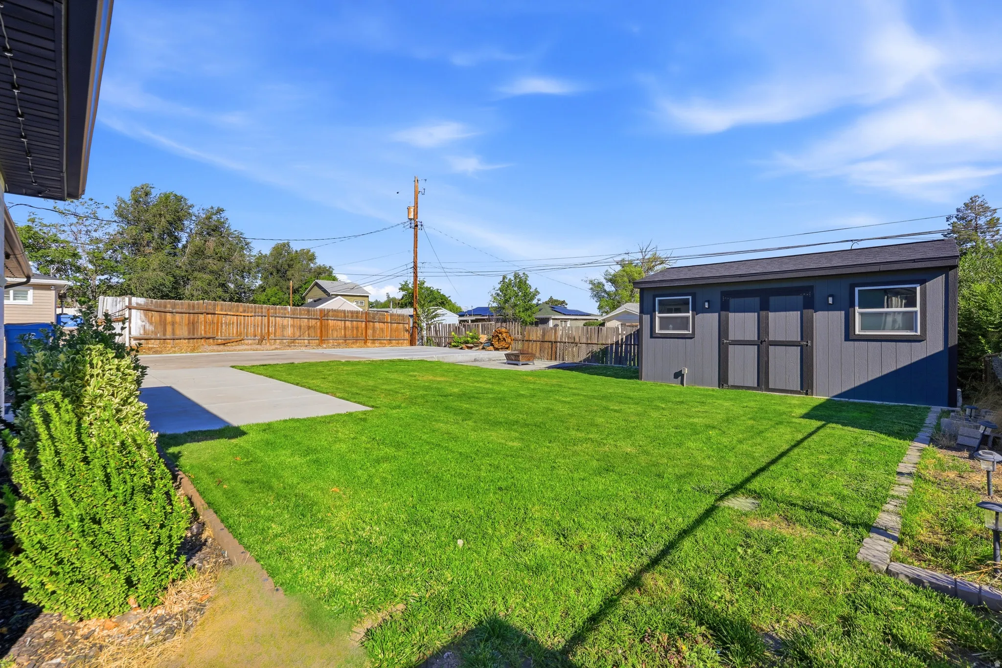 Expansive green lawn with a privacy fence, concrete patio, and a detached shed