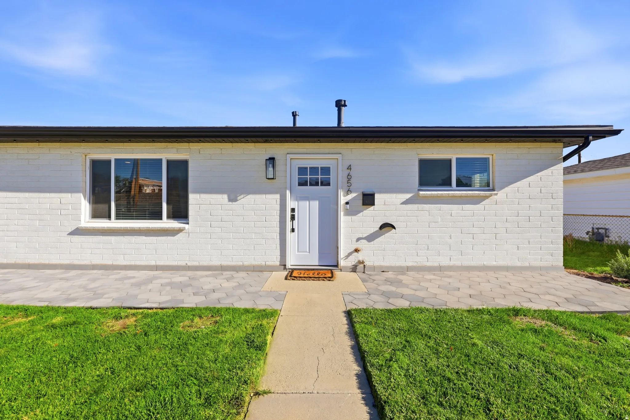 White brick facade with black trim, entryway with a white door and sidelight, and a paved patio area