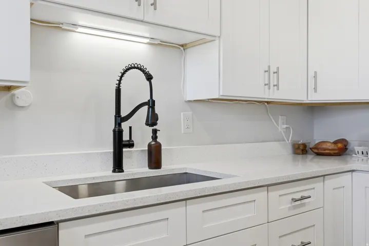 White shaker-style cabinetry with brushed nickel hardware, light-toned speckled countertops, undermount stainless steel sink, and a matte black pull-down faucet