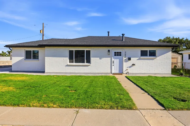 White brick exterior with a dark shingle roof, a white entry door, and a concrete pathway