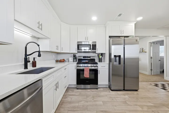 Modern kitchen featuring white cabinetry, light countertops, wood-finish flooring, a stainless steel refrigerator, and a matte black faucet