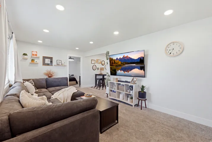 Recessed ceiling lighting, light-toned carpeting, white wall finishes, and a dark wood-finish coffee table