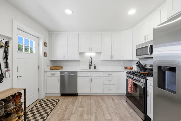 White shaker-style cabinetry with matte black hardware, stainless steel appliances, wood-finish flooring, and a glass-paneled door
