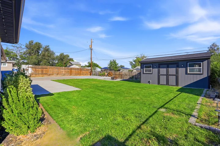 Expansive green lawn with a privacy fence, concrete patio, and a detached shed
