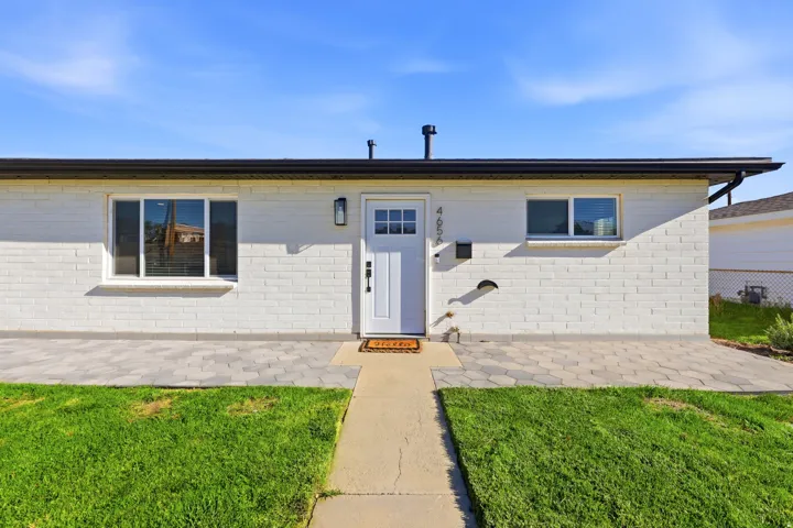 White brick facade with black trim, entryway with a white door and sidelight, and a paved patio area
