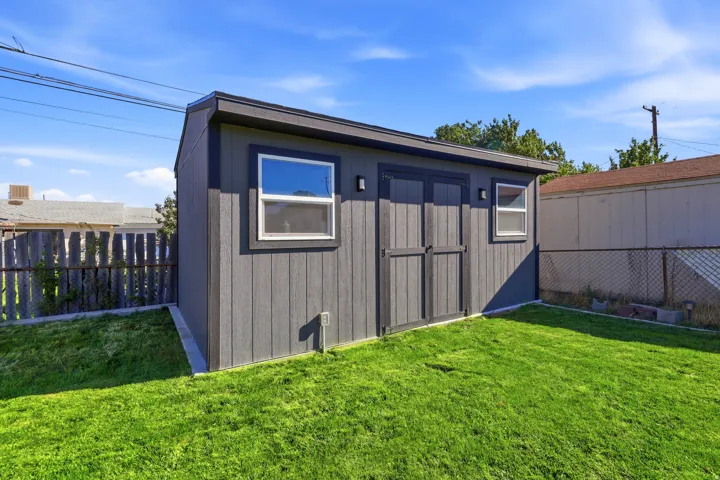 Detached shed with double doors, two windows, and a sloped roof, set on a manicured lawn