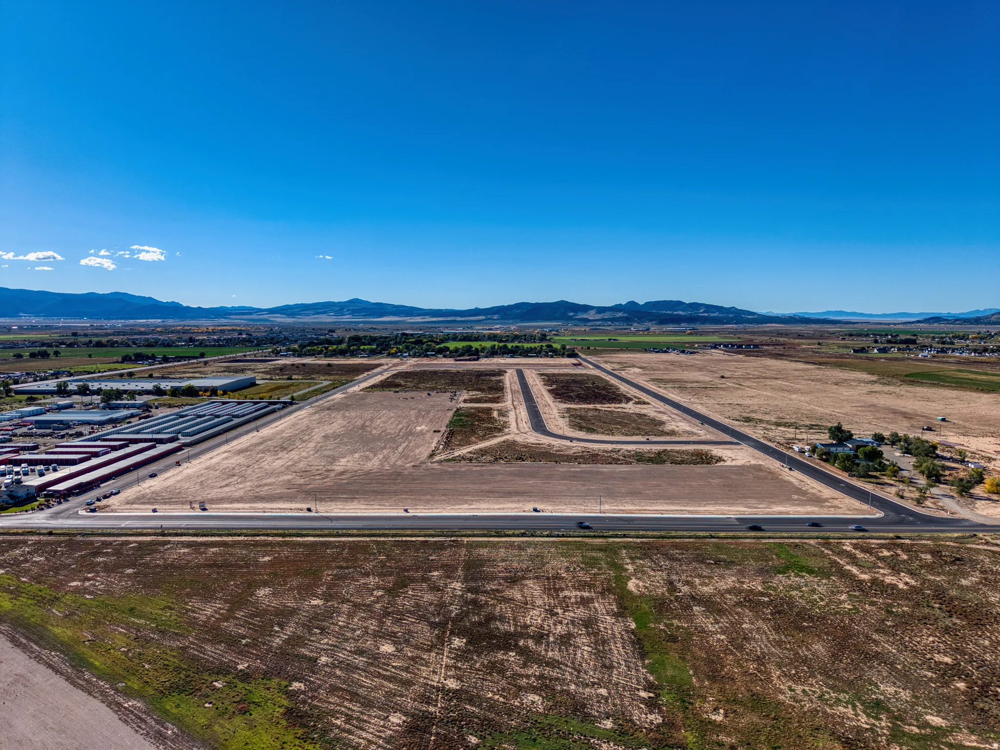 Expansive undeveloped land featuring a clear sky, distant mountain range, and a paved roadway