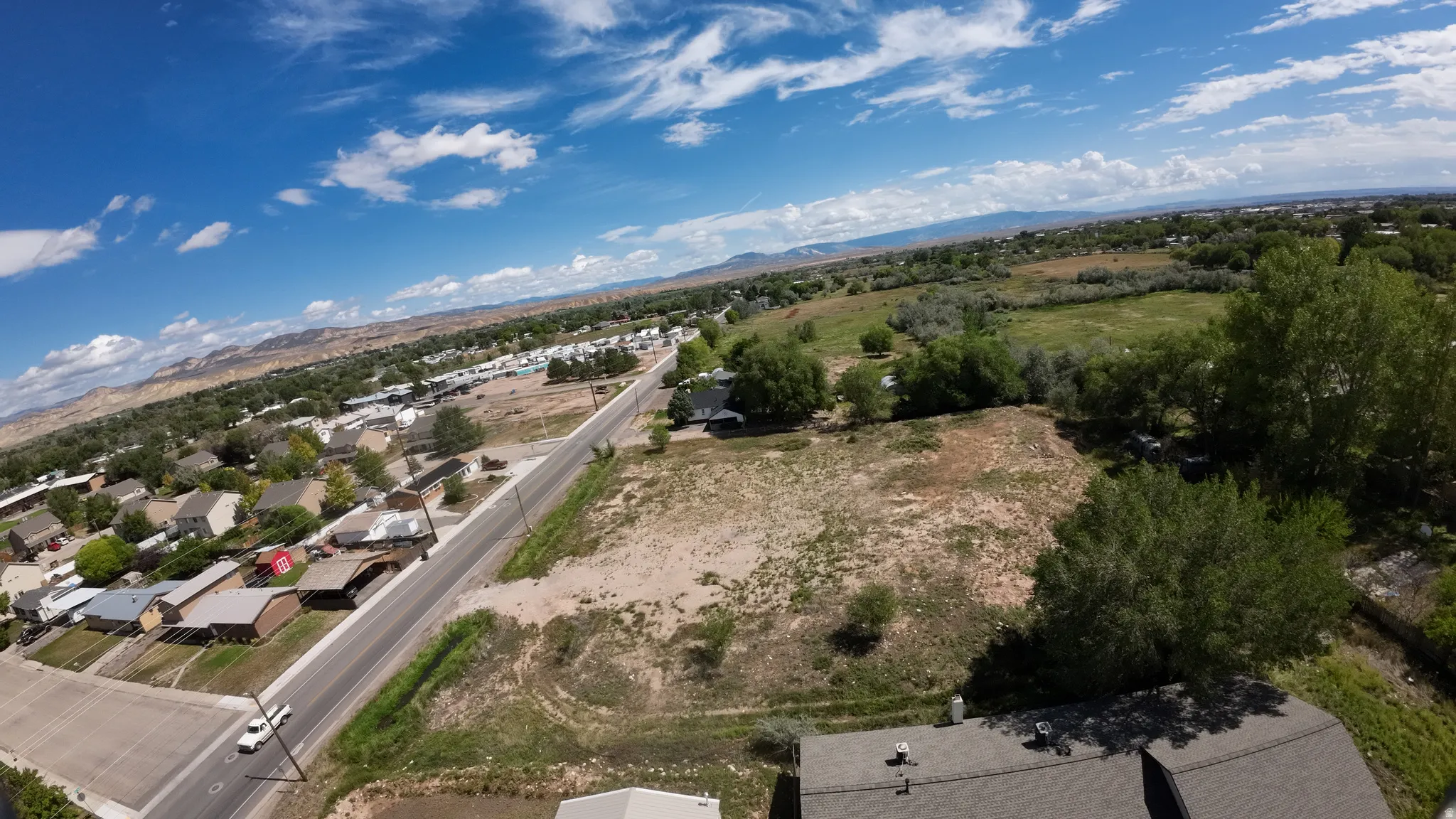Expansive lot featuring mature trees, a paved road, and distant mountain scenery