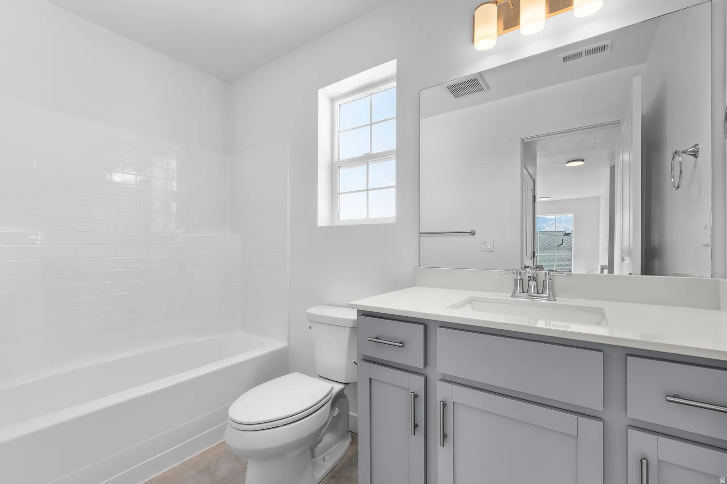 Bathroom featuring a white subway tile tub surround, window, light gray cabinetry, and a vanity with a rectangular sink and chrome fixtures