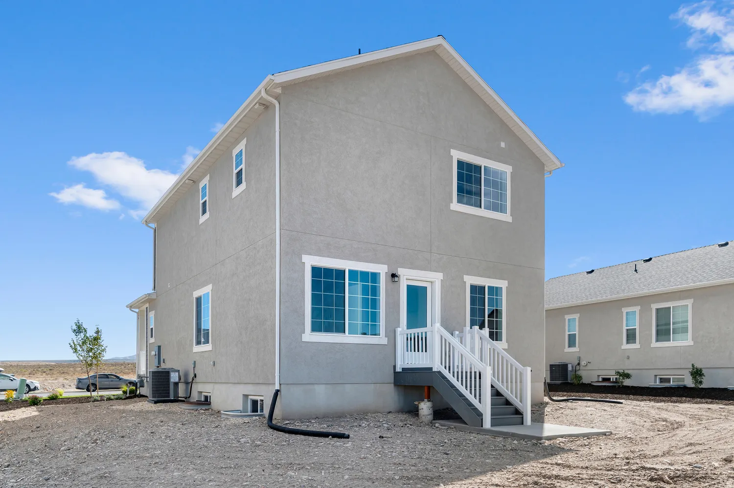 Stucco exterior with white trim, multiple windows, and exterior stairs leading to a concrete pad