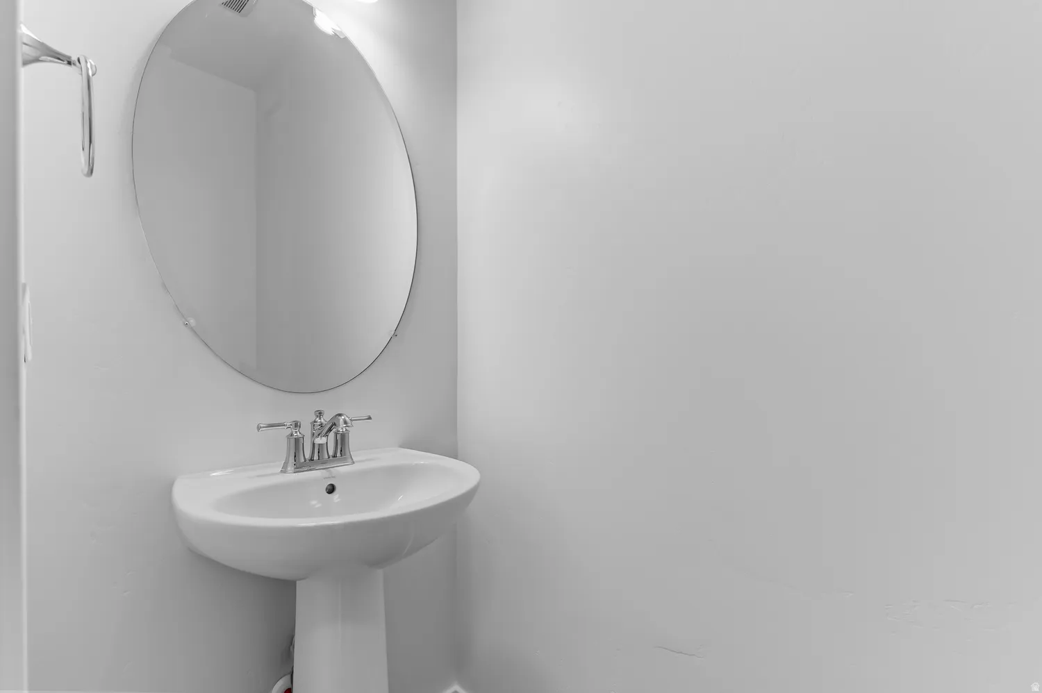 Pedestal sink with chrome hardware and an oval wall mirror