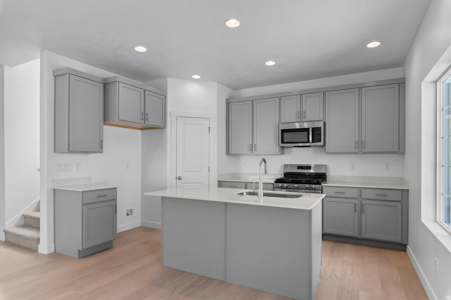 Kitchen featuring light gray cabinetry, stainless steel appliances, a center island with sink, light countertops, and wood-finish flooring