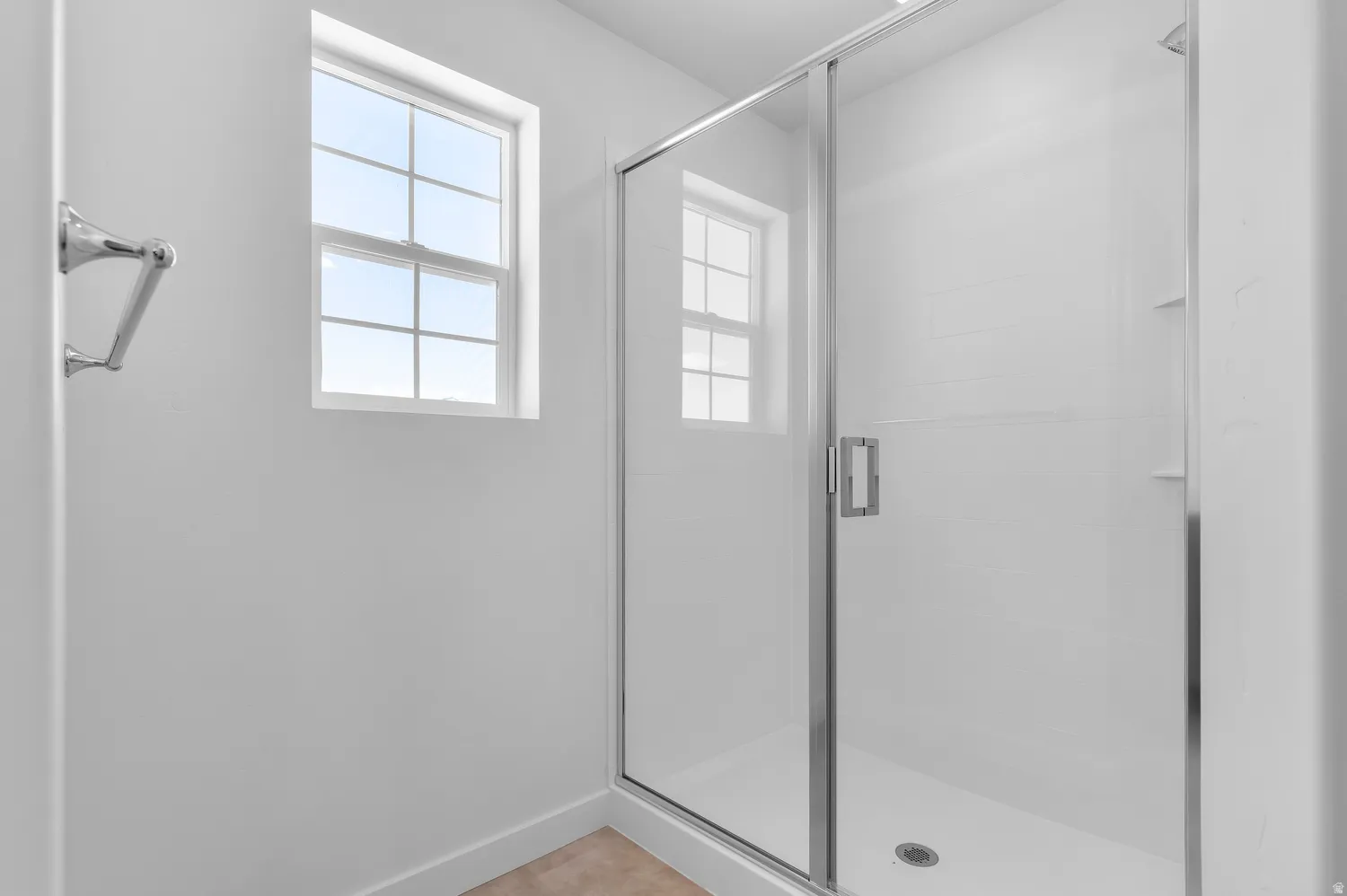Glass-enclosed shower with white tiled walls, built-in shelving, and a chrome towel bar