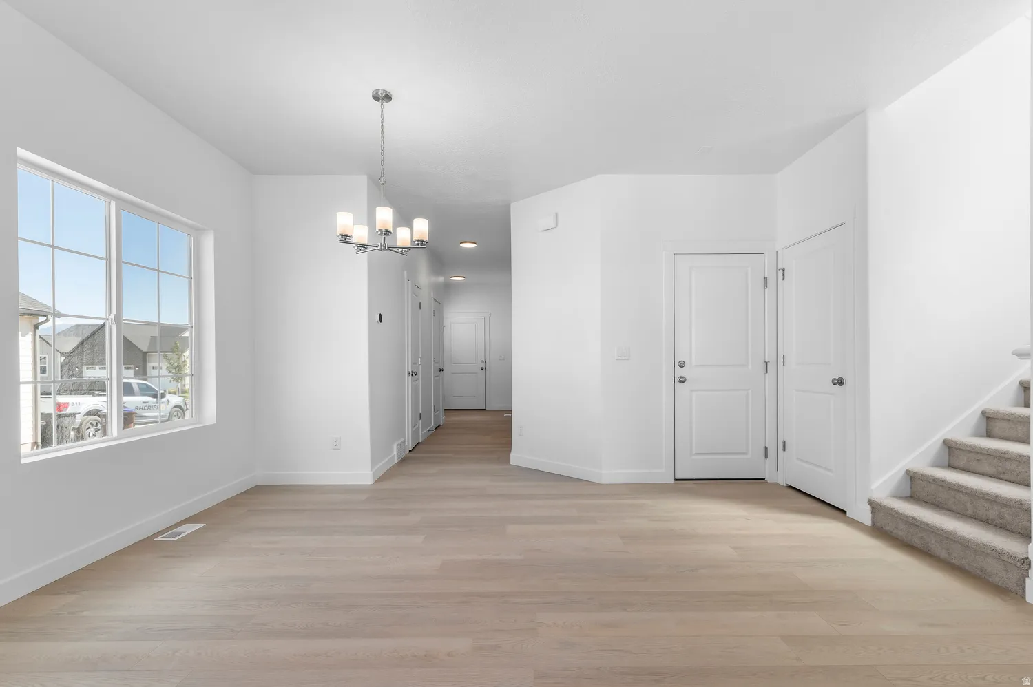 Expansive room with wood-finish flooring, large window with grid panes, and a modern chandelier