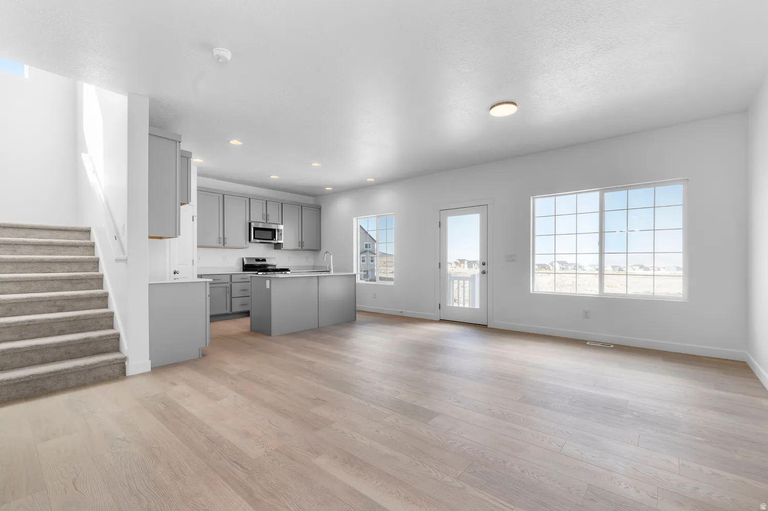 Open-concept living area featuring wood-finish flooring, a kitchen island, recessed lighting, and large windows