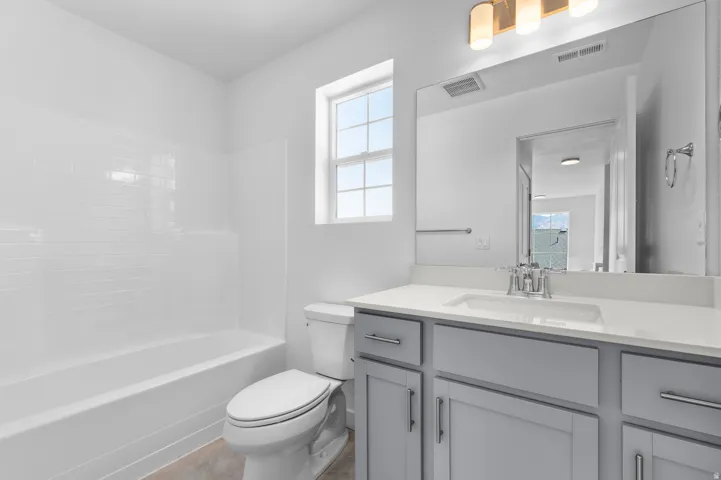Bathroom featuring a white subway tile tub surround, window, light gray cabinetry, and a vanity with a rectangular sink and chrome fixtures
