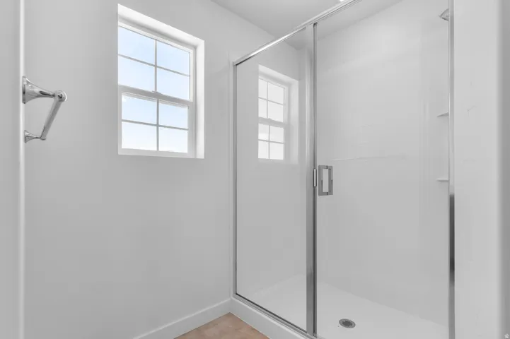 Glass-enclosed shower with white tiled walls, built-in shelving, and a chrome towel bar