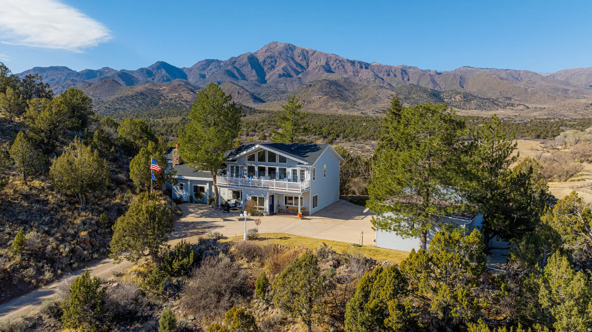 Two-story residence featuring a balcony, attached garage, and a detached outbuilding, set against a backdrop of mountainous terrain