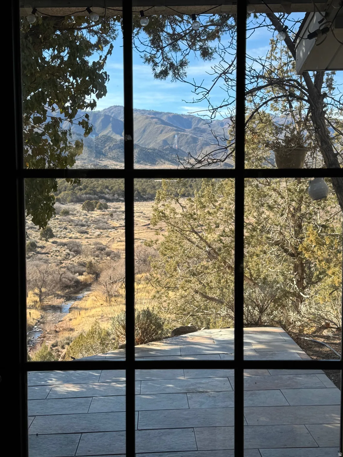 Large pane window framing a mountain landscape, natural terrain, and a visible stream