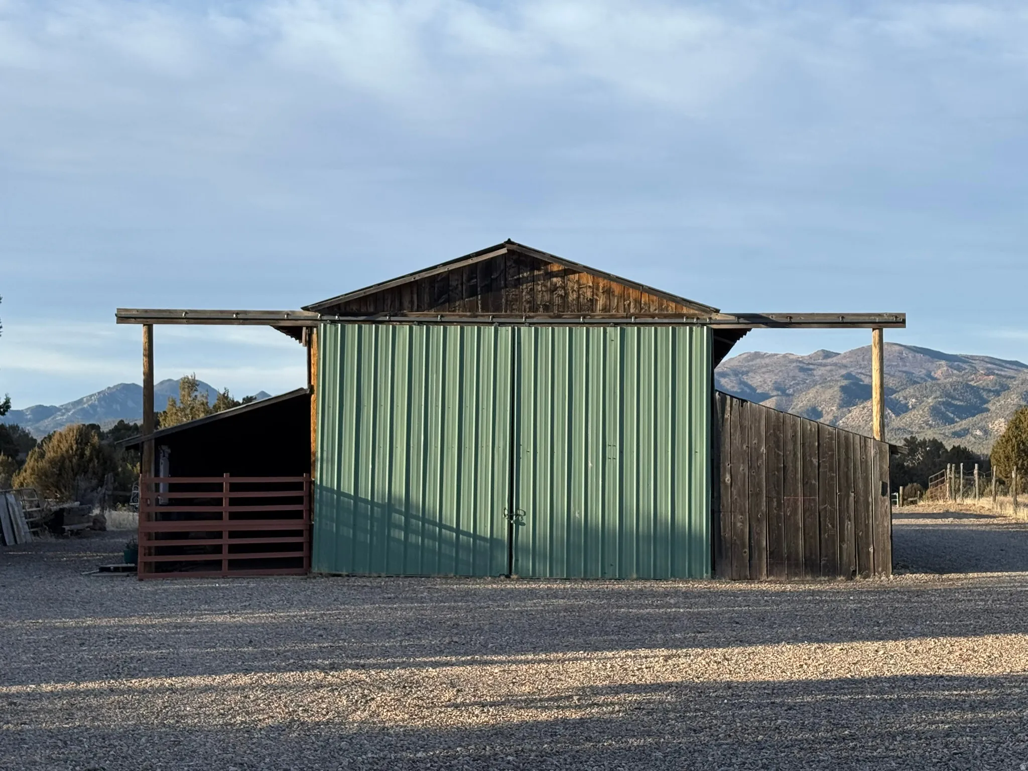 Barn structure featuring green metal siding, natural wood accents, a sloped roof, and an open-sided extension