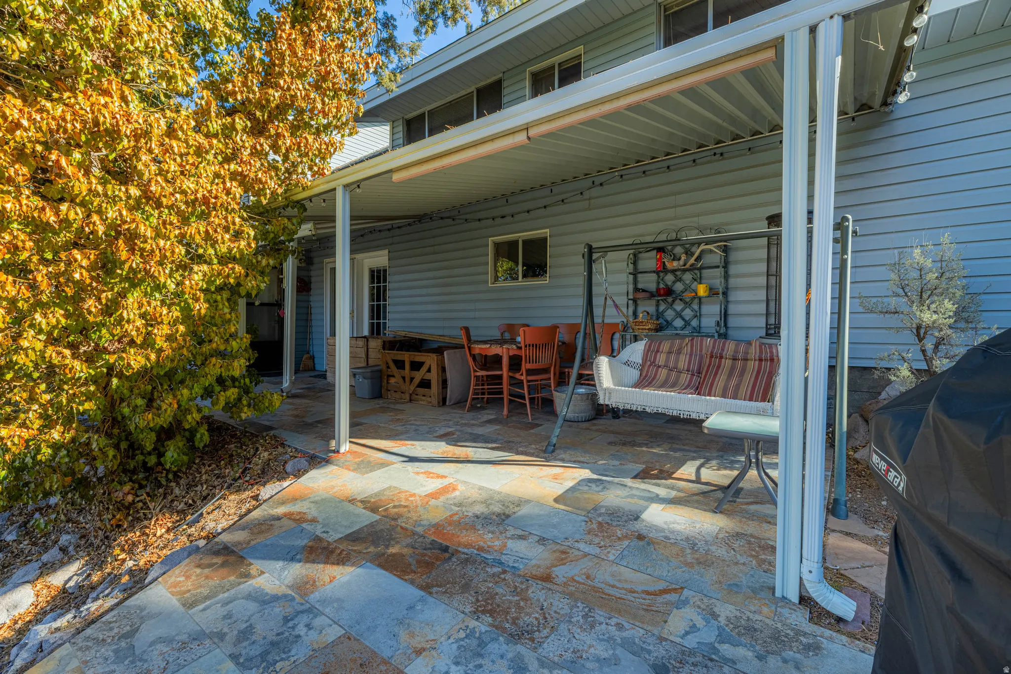 Patio featuring multi-color stone pavers, a light blue siding exterior, a white metal awning, and multiple windows
