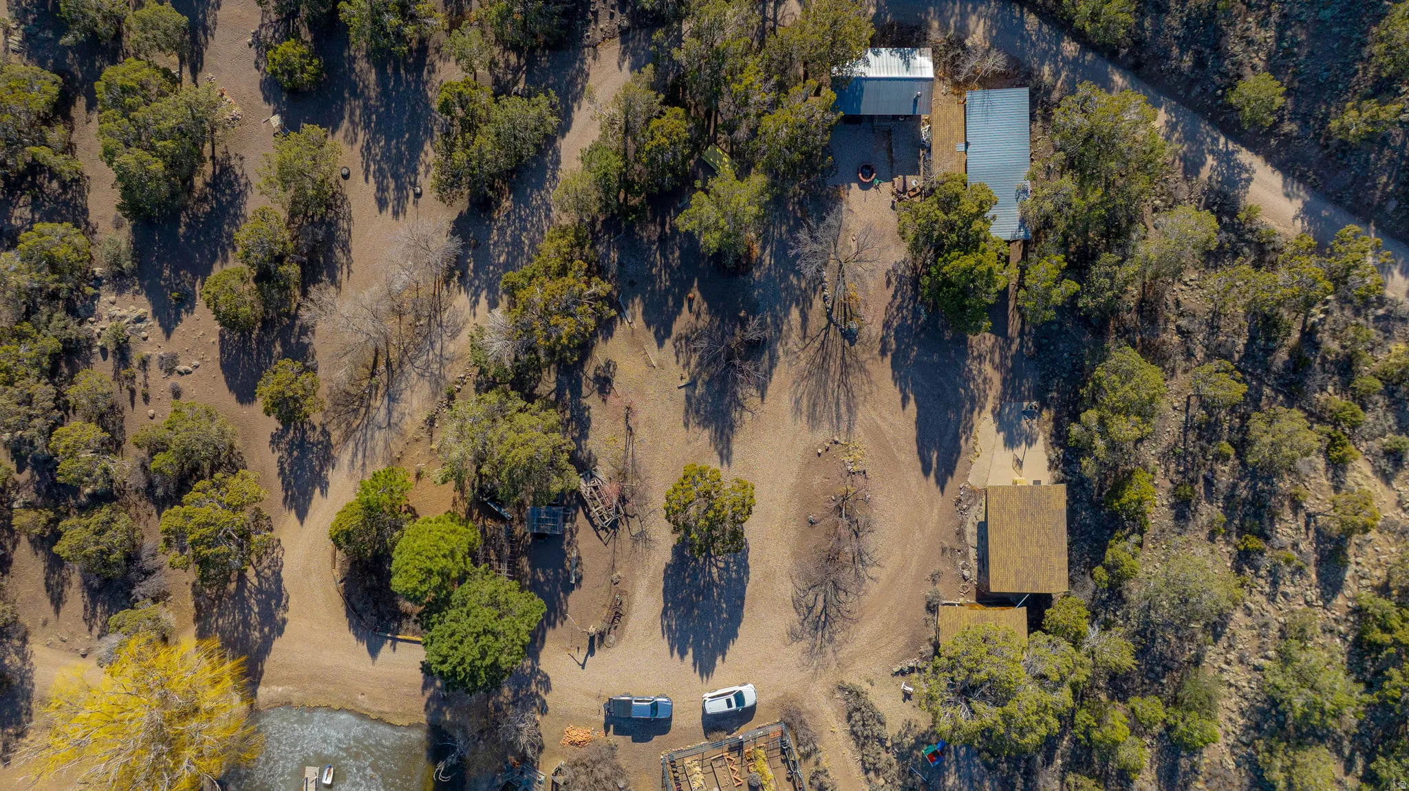 Expansive property featuring dense tree coverage, a natural body of water, and multiple structures with distinct roofing materials