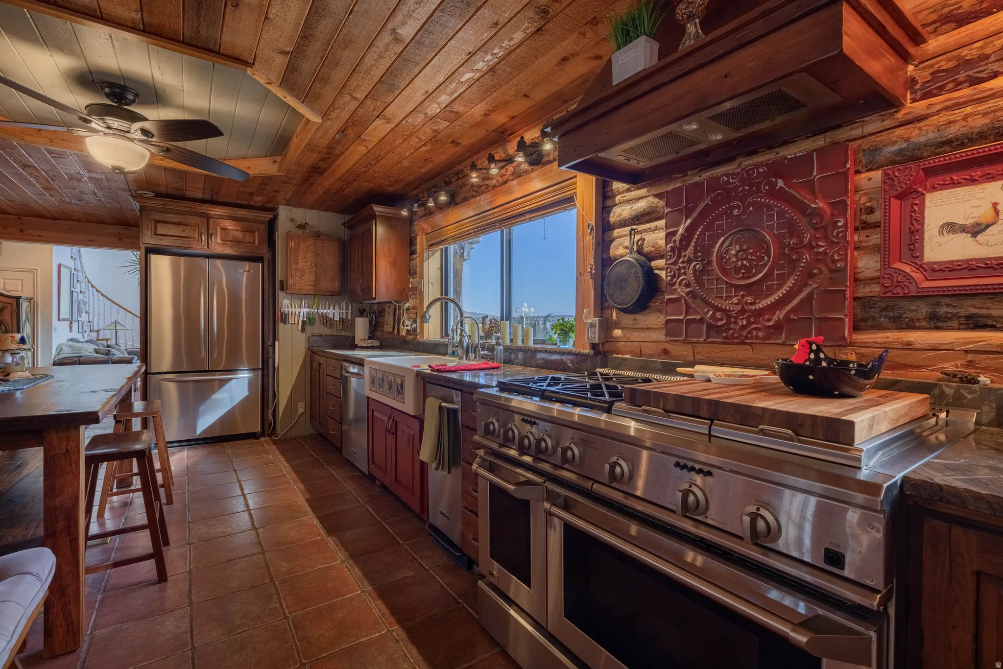 Wood plank ceiling, log wall construction, stainless steel appliances, farmhouse sink, and terracotta tile flooring