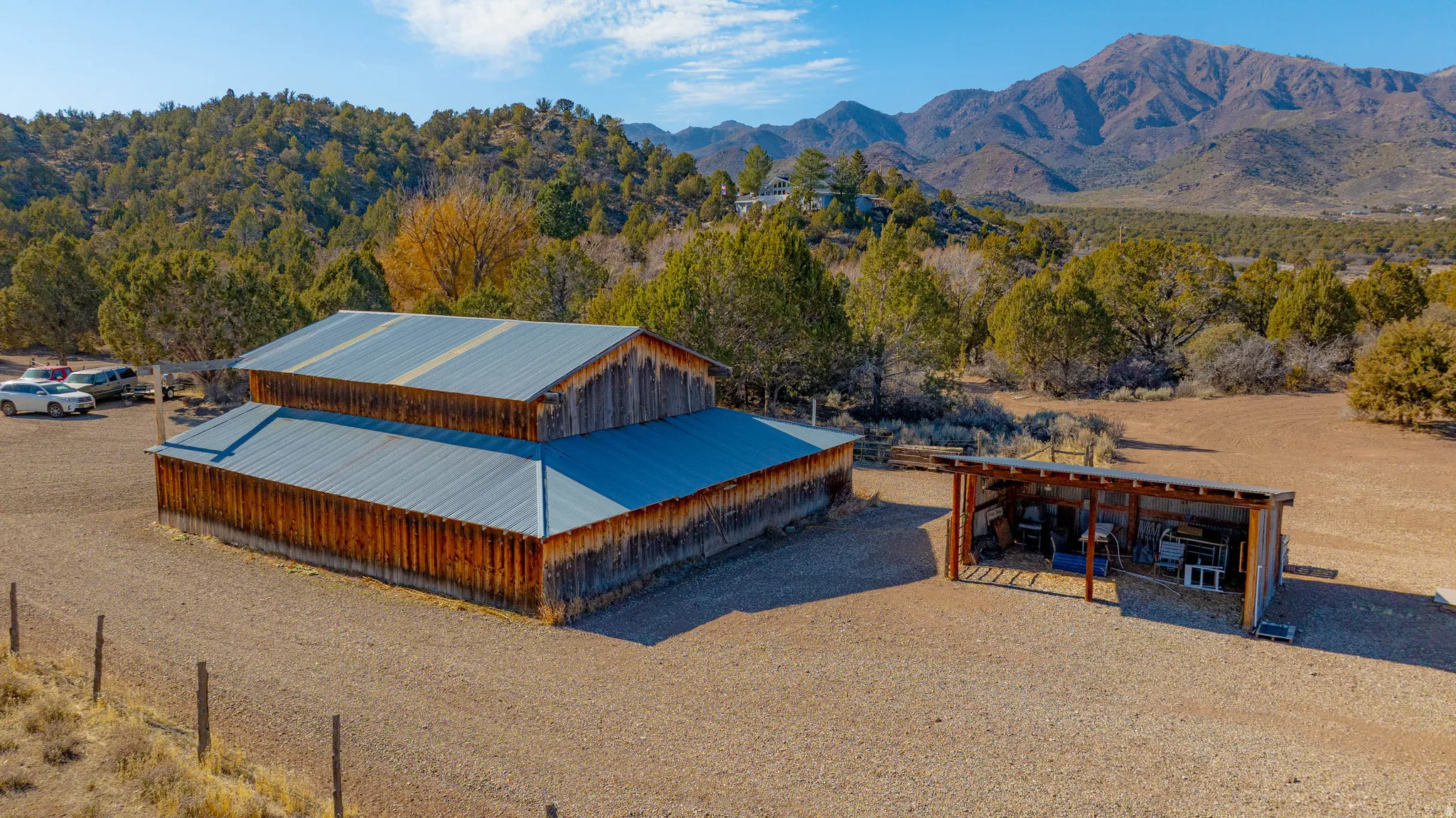 Expansive property featuring a two-story barn with metal roofing, an open-sided storage structure, and a natural, unlandscaped terrain