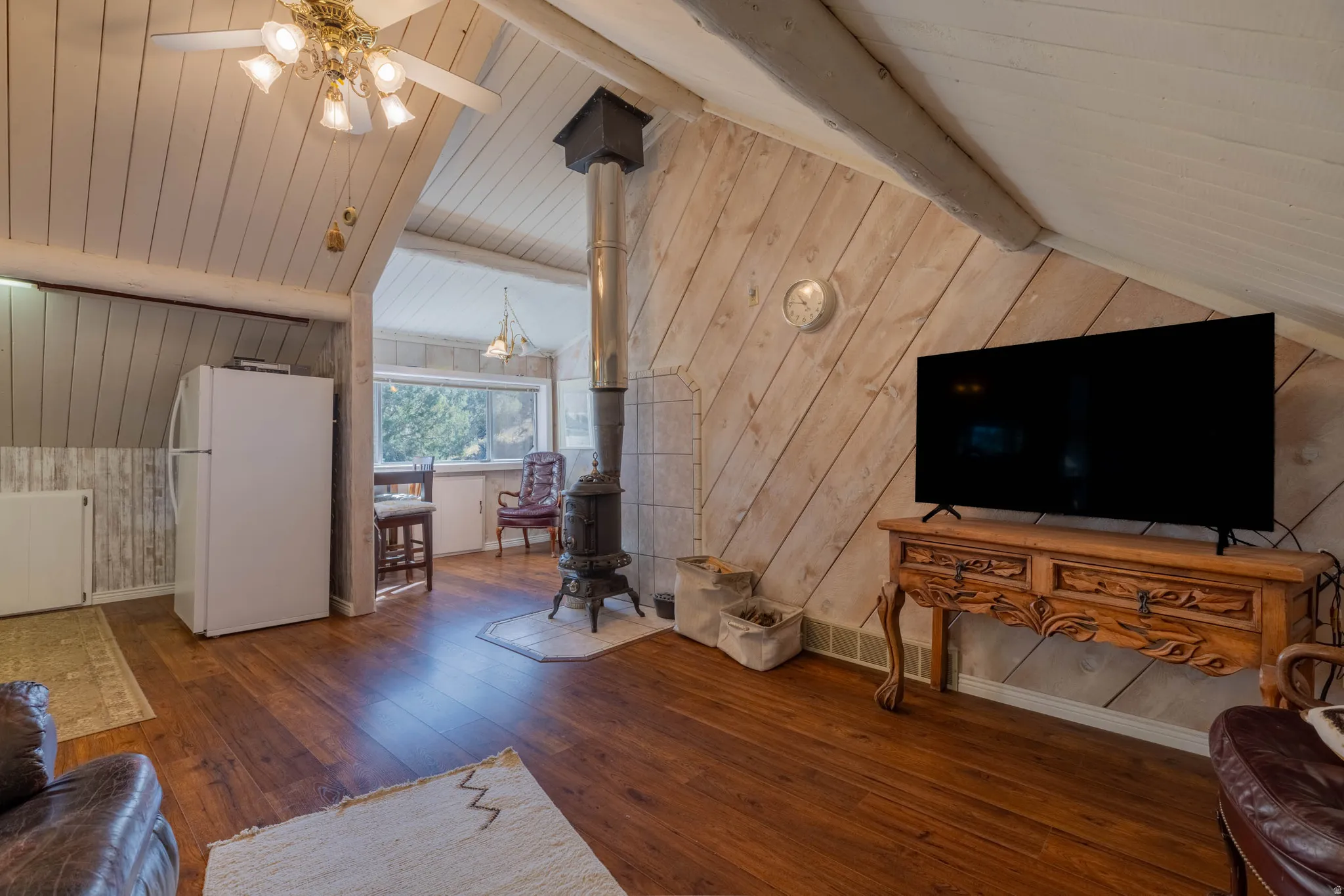 Wood-finish flooring throughout, featuring a cast-iron wood stove with a stone hearth, exposed ceiling beams, and paneled walls