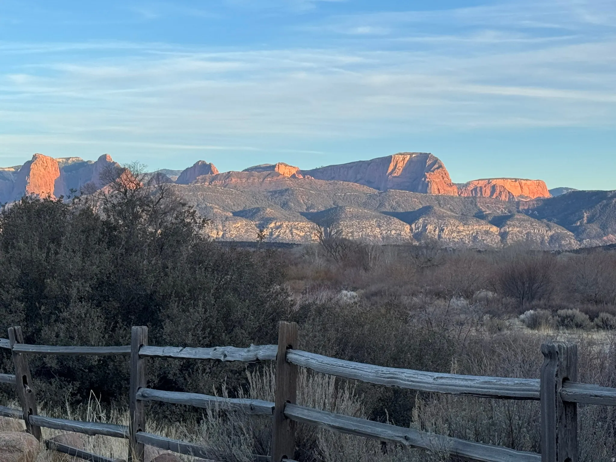 Rustic wooden fence line with a natural landscape backdrop, featuring distant red rock formations and expansive blue sky
