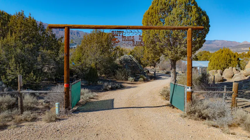Gravel driveway with a rustic wooden entryway, surrounded by natural landscaping and mature trees