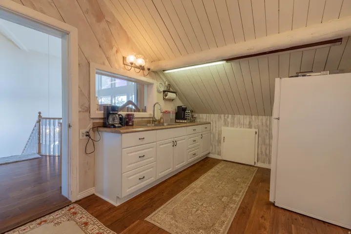 White cabinetry, wood-finish flooring, accent wall paneling, sloped planked ceiling, and a wall-mounted light fixture