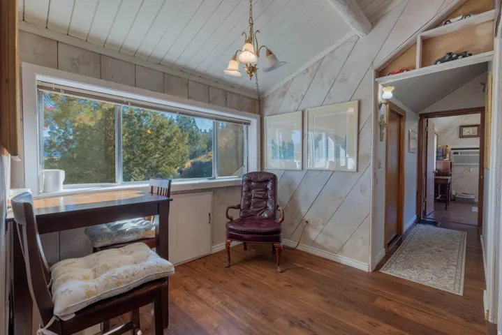 Vaulted ceiling with exposed beams, wood-finish flooring, horizontal window, built-in shelving, and wood paneling