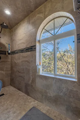 Tiled shower with an arched window, a decorative tile accent band, recessed lighting, and a rainfall showerhead