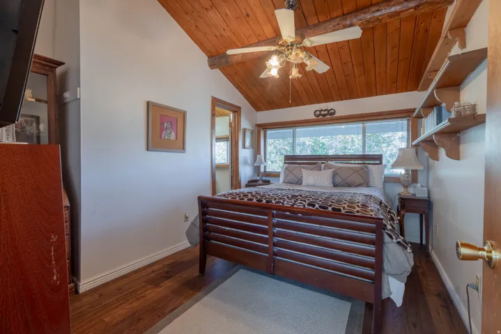 Vaulted wood-paneled ceiling with exposed beam, wood-finish flooring, a large window, and built-in shelving
