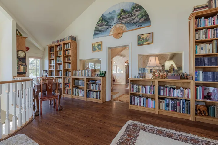 Vaulted ceiling, wood-finish flooring, built-in shelving, white balustrade, and a window with natural light