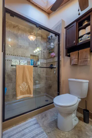 Glass-enclosed shower with tile surround, built-in wall cabinet, and wood-paneled ceiling with a ceiling fan