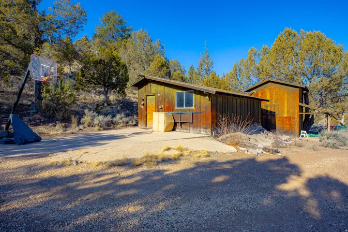 Modern cabin-style residence featuring warm wood-finish exterior with large picture windows, situated on a generously sized lot surrounded by mature pine and aspen trees