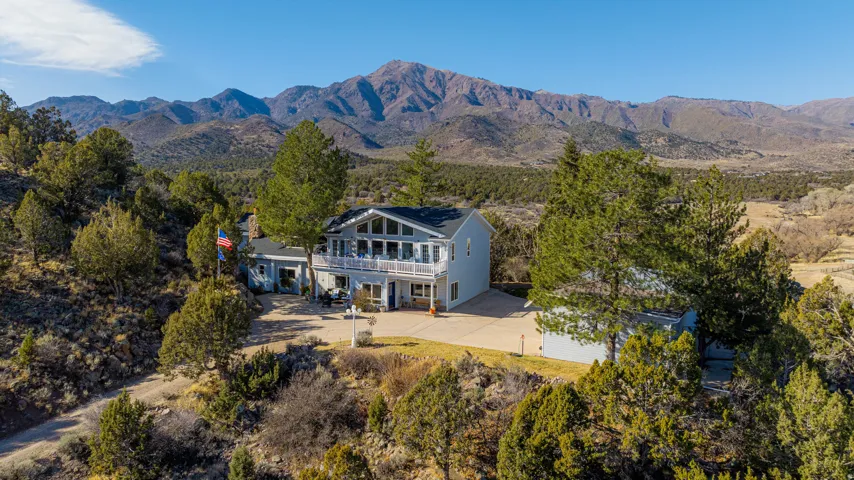 Two-story residence featuring a balcony, attached garage, and a detached outbuilding, set against a backdrop of mountainous terrain