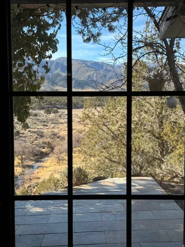 Large pane window framing a mountain landscape, natural terrain, and a visible stream
