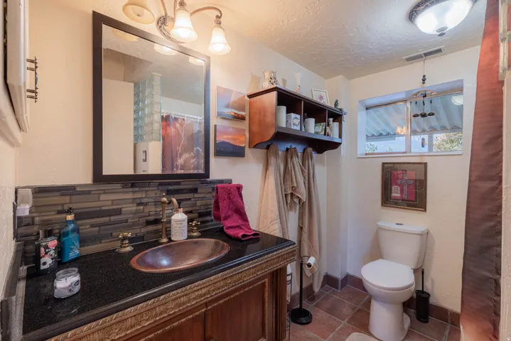 Vanity with an oval vessel sink, dark countertop, and tiled backsplash