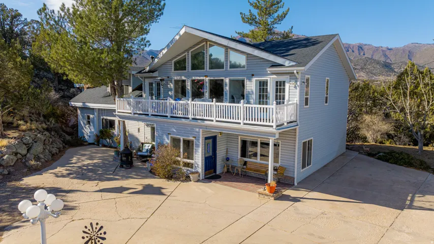 Multi-level home featuring light blue siding, a white balcony with railing, an expansive concrete driveway, and prominent mountain scenery in the background
