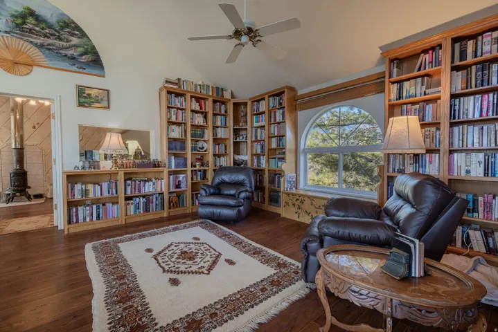 Sophisticated library retreat showcasing extensive built-in wood cabinetry with integrated bookshelves spanning multiple walls, hardwood flooring throughout, arched transom window with natural light, and ceiling fan with brushed-metal finish
