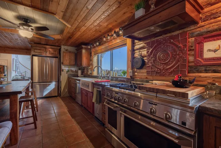 Wood plank ceiling, log wall construction, stainless steel appliances, farmhouse sink, and terracotta tile flooring