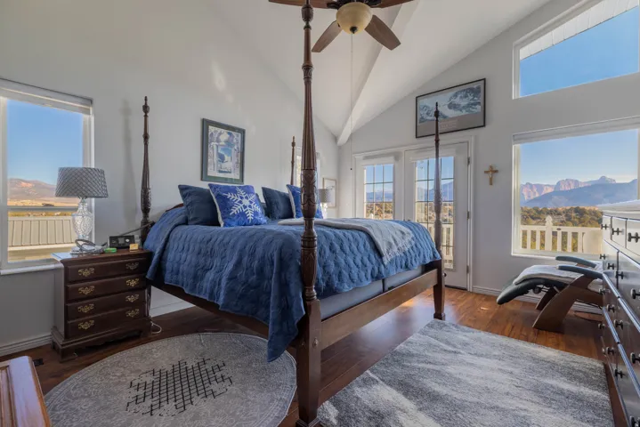 Vaulted ceiling with a ceiling fan, wood-finish flooring, multiple windows, and exterior double doors