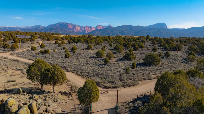 Expansive property featuring a rustic gate, natural desert landscaping, and distant mountain ranges