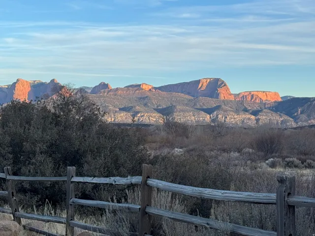 Rustic wooden fence line with a natural landscape backdrop, featuring distant red rock formations and expansive blue sky